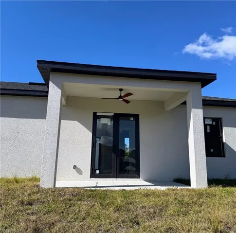 View of exterior entry featuring a ceiling fan, a yard, and stucco siding