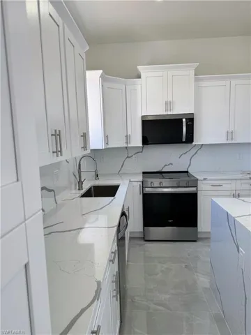 Kitchen featuring stainless steel appliances, light stone countertops, white cabinets, and backsplash