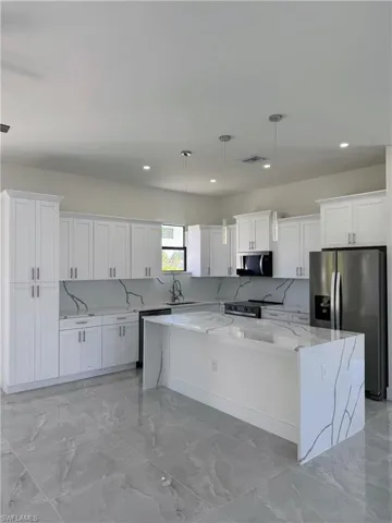 Kitchen with backsplash, light stone countertops, stainless steel appliances, a large island, and decorative light fixtures