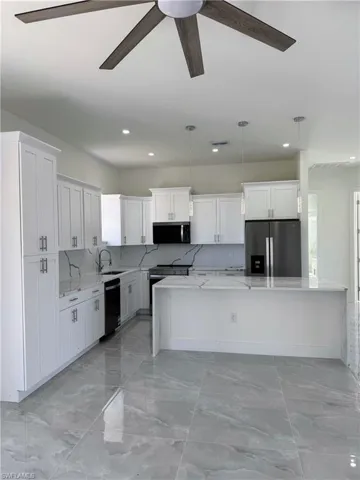 Kitchen with ceiling fan, light stone counters, a spacious island, stainless steel appliances, and backsplash