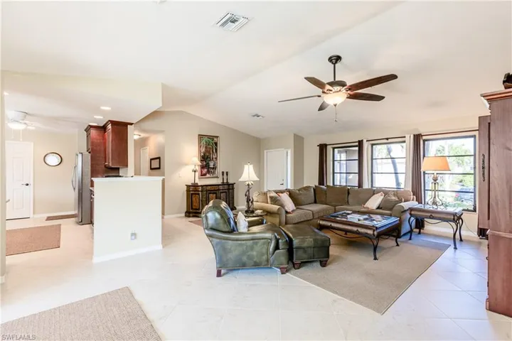Living room with light tile patterned floors, visible vents, baseboards, ceiling fan, and vaulted ceiling