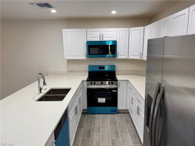 Kitchen featuring appliances with stainless steel finishes, white cabinetry, light stone counters, and recessed lighting