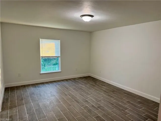 Unfurnished room with baseboards and dark wood-style floors