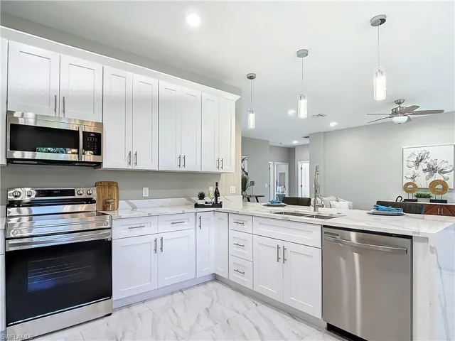 Kitchen with white cabinets, appliances with stainless steel finishes, light tile floors, and kitchen peninsula