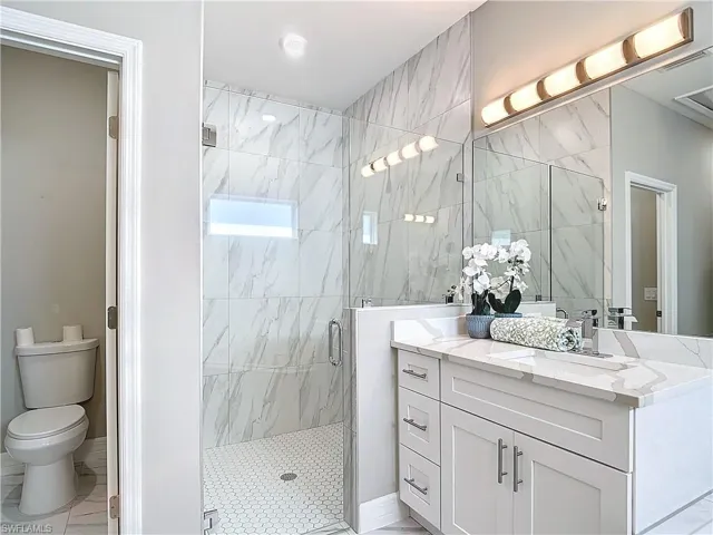Bathroom with tile walls, walk in shower, tile floors, toilet, and large vanity