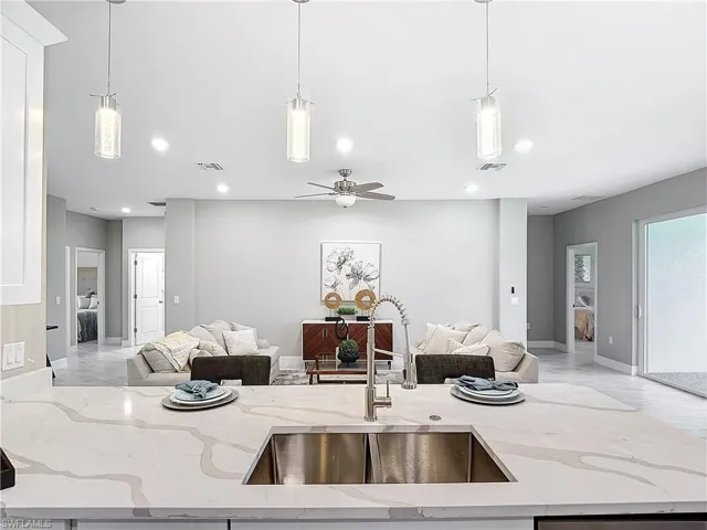 Kitchen with hanging light fixtures, light stone countertops, sink, and ceiling fan