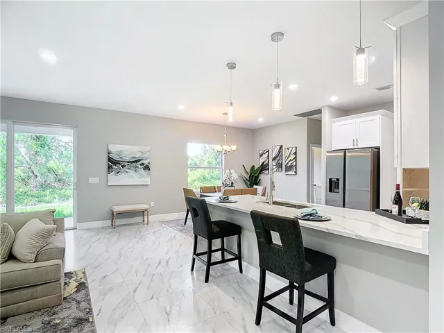 Kitchen featuring white cabinetry, stainless steel fridge with ice dispenser, hanging light fixtures, a breakfast bar area, and light stone counters