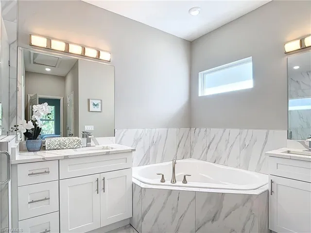 Bathroom with tiled bath, plenty of natural light, and double sink vanity