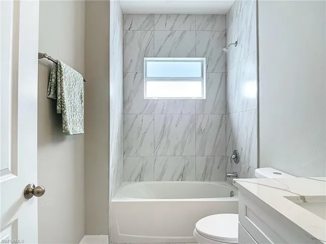 Full bathroom with tiled shower / bath combo, vanity, and toilet