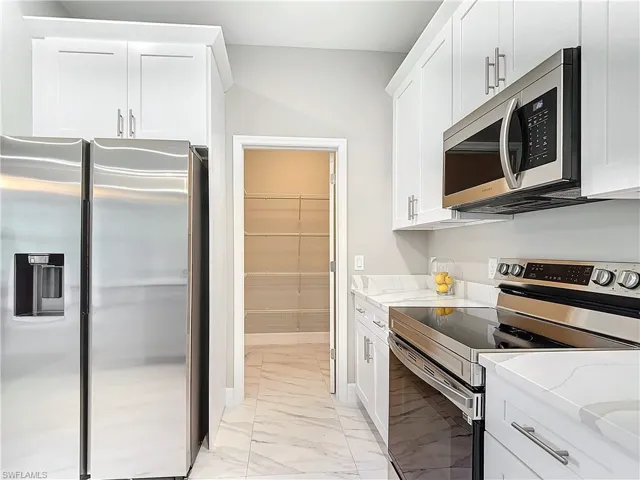 Kitchen with light stone countertops, stainless steel appliances, white cabinets, and light tile floors
