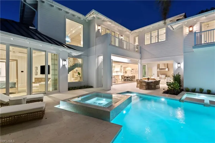 Back house at twilight featuring a pool with hot tub, a patio, and a balcony