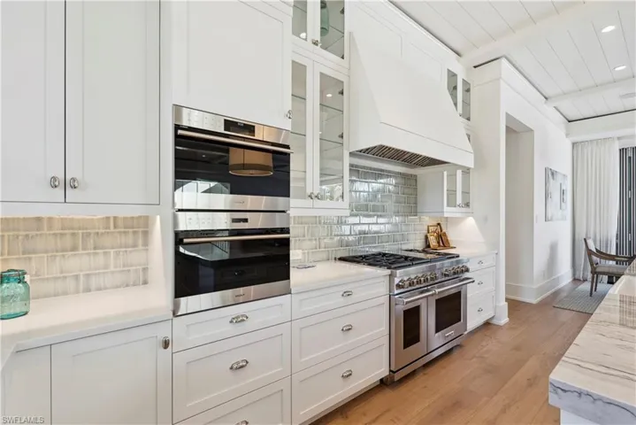 Kitchen featuring white cabinetry, tasteful backsplash, stainless steel appliances, and custom range hood