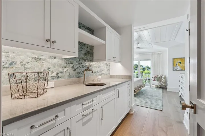 Kitchen with light stone countertops, sink, white cabinets, and light hardwood / wood-style floors