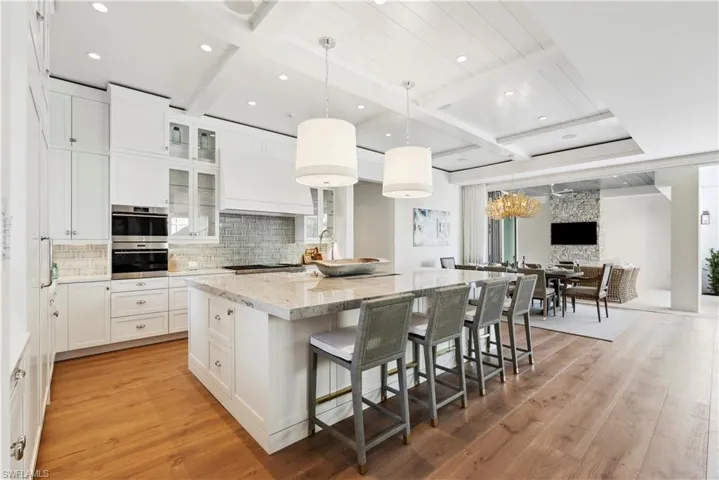 Kitchen with light stone countertops, decorative light fixtures, white cabinets, and a spacious island