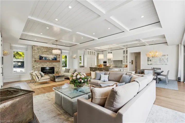 Living room featuring coffered ceiling, a stone fireplace, light hardwood / wood-style flooring, a notable chandelier, and beam ceiling