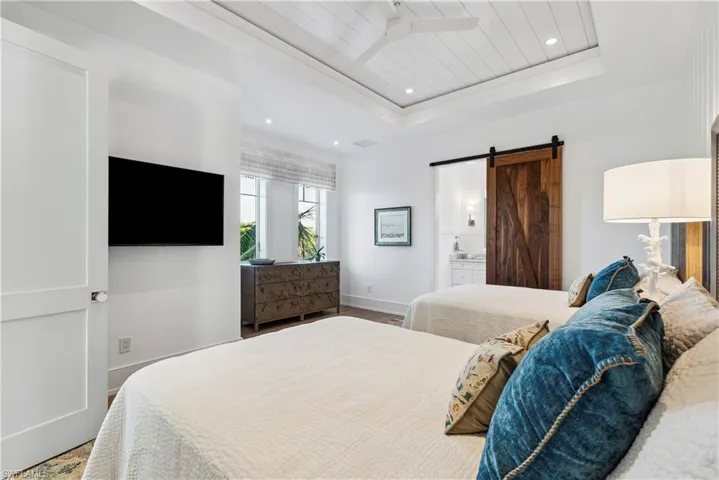Bedroom featuring wood-type flooring, a barn door, connected bathroom, and a tray ceiling