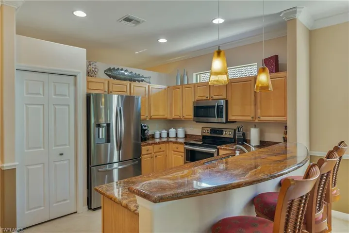 Kitchen with dark stone countertops, stainless steel appliances, a peninsula, hanging light fixtures, and ornamental molding
