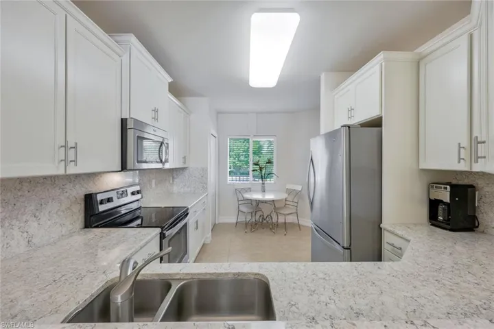 Kitchen with tasteful backsplash, light tile flooring, sink, white cabinets, and appliances with stainless steel finishes