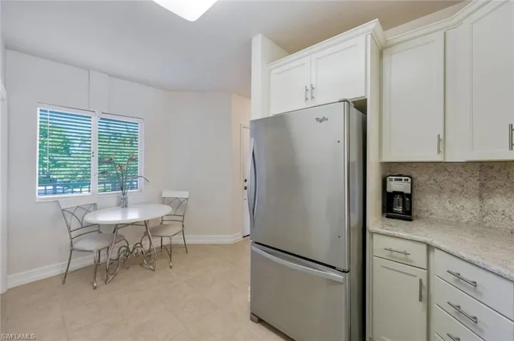 Kitchen featuring light stone countertops, stainless steel fridge, white cabinets, backsplash, and light tile floors