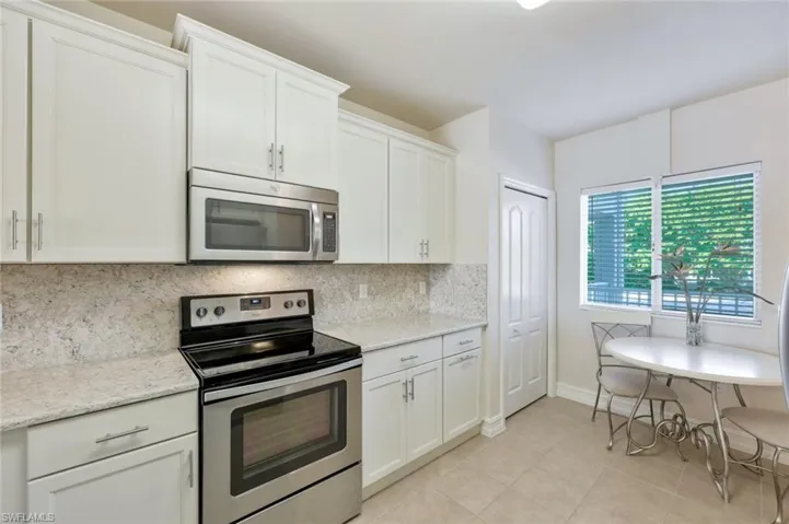 Kitchen with light stone countertops, backsplash, light tile floors, and stainless steel appliances