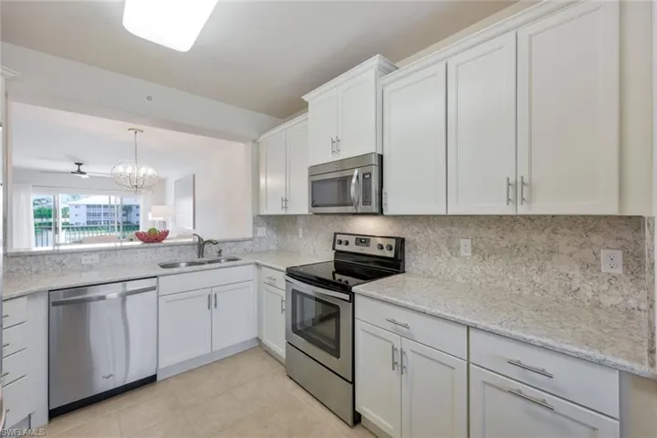 Kitchen featuring stainless steel appliances, backsplash, light tile floors, sink, and white cabinetry