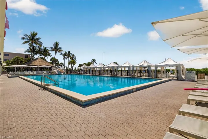 Expansive outdoor pool area featuring a rectangular pool, paver decking, multiple private cabanas, and tropical landscaping