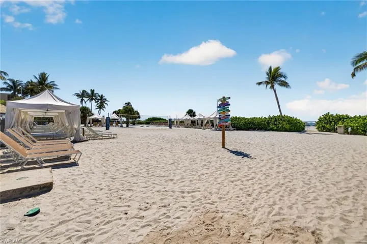 Expansive sandy beach featuring cabana seating, palm trees, and lush green foliage