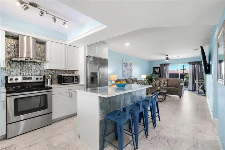 Kitchen featuring white cabinetry, stainless steel appliances, a CUSTOM Porcelain countertop island with tiled paneling, multicolored glass tile backsplash, and recessed track lighting