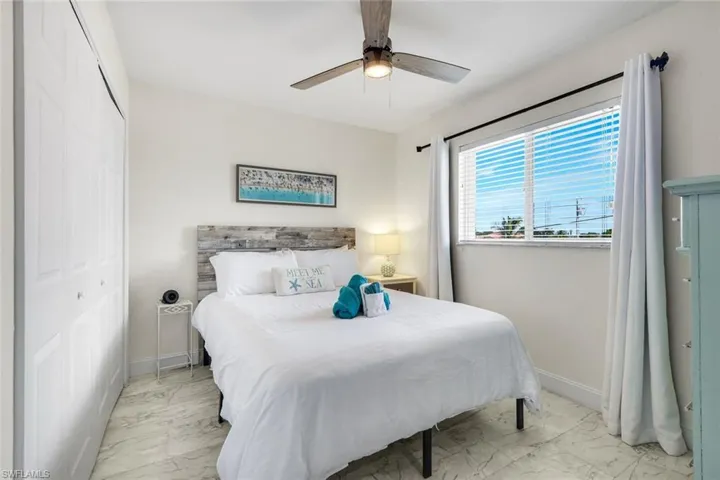 Neutral-toned interior featuring, white-panel reach-in closet, integrated ceiling fan with light fixture, and large window with blinds