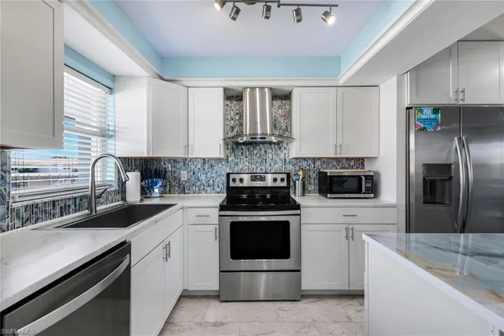 Kitchen featuring white shaker-style cabinetry, stainless steel appliances, patterned glass tile backsplash, stone-surface countertops