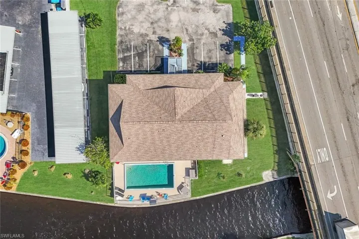 Aerial perspective featuring a NEWER (2023) shingled hipped roof, rectangular swimming pool, concrete paved, and manicured green space bordering a canal