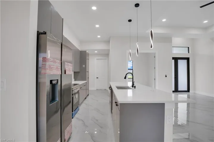Kitchen with gray cabinetry, sink, stainless steel fridge with ice dispenser, pendant lighting, and a center island with sink