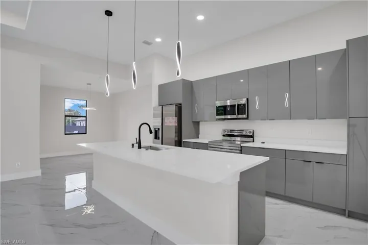 Kitchen featuring gray cabinetry, a center island with sink, sink, decorative light fixtures, and stainless steel appliances