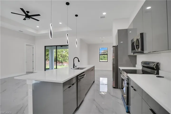 Kitchen with gray cabinetry, a center island with sink, hanging light fixtures, sink, and appliances with stainless steel finishes