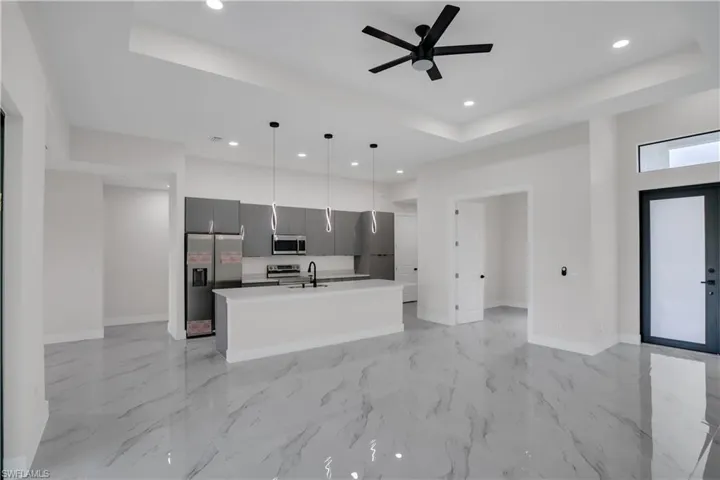 Kitchen with a kitchen island with sink, hanging light fixtures, ceiling fan, appliances with stainless steel finishes, and a tray ceiling