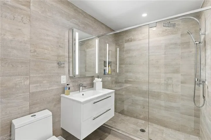 Fully tiled bathroom with a frameless glass shower enclosure, a wall-mounted vanity with integrated sink, and an illuminated mirrored medicine cabinet