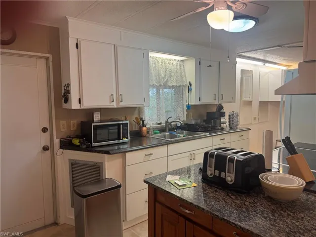 Kitchen featuring white cabinetry with brushed nickel hardware, speckled countertops, a double basin stainless steel sink, and a central wood-finish island with a matching speckled countertop