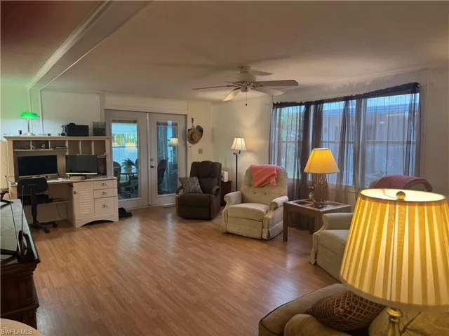 Living area featuring wood-finish flooring, a ceiling fan with integrated lighting, and multiple windows