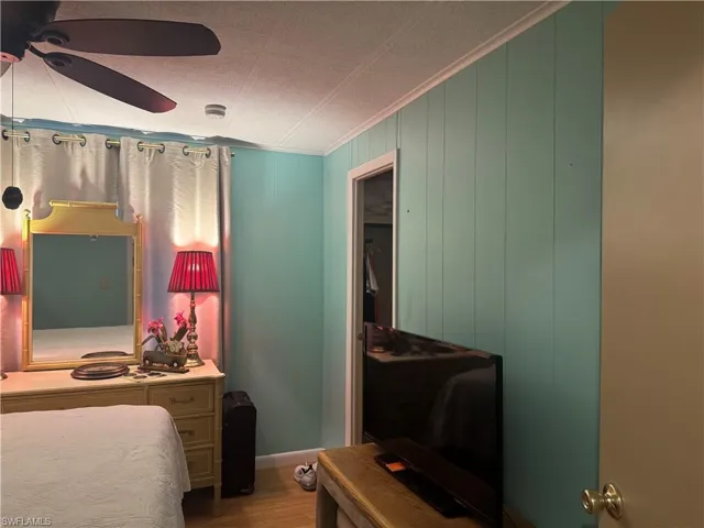 Interior room featuring vertical paneling, light wood-finish flooring, a ceiling fan, and crown molding