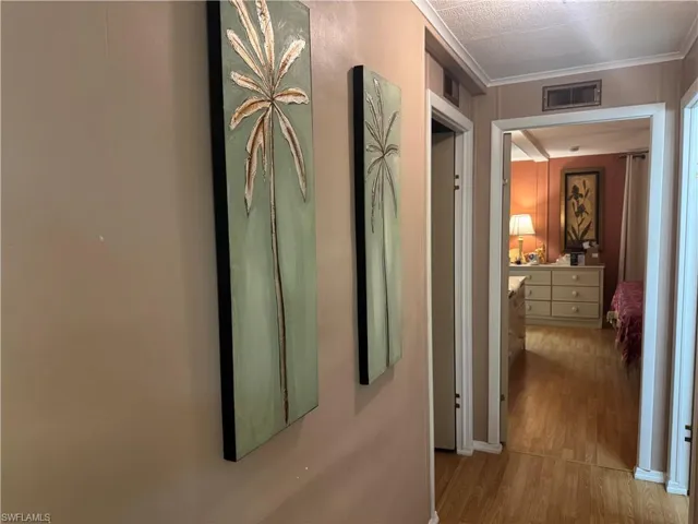 Hallway featuring wood-finish flooring, crown molding, and two ceiling vents