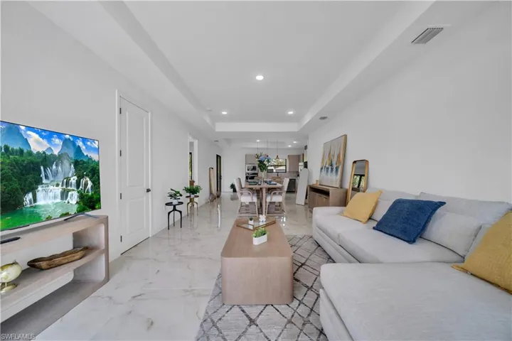Open-concept living area with large-format white tile flooring and recessed lighting