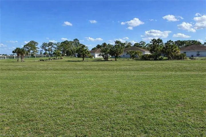Expansive green field featuring a clear blue sky, distant houses, and mature trees