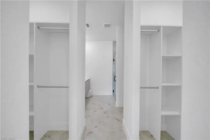 Walk-through closet featuring dual hanging rods, integrated shelving, white cabinetry, and light-toned tile flooring