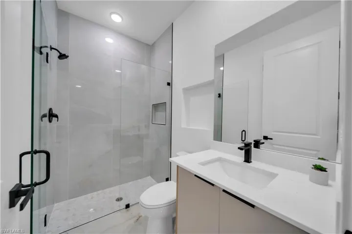 Walk-in shower with clear glass enclosure and gray tile surround, featuring matte black fixtures