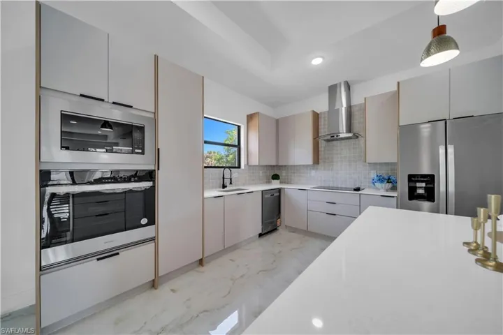Modern kitchen featuring white cabinetry, integrated stainless steel appliances, a white island, and a tiled backsplash