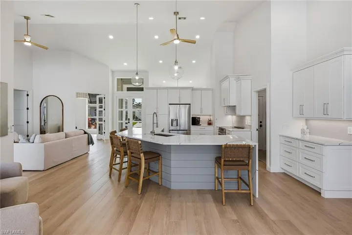 Kitchen with ceiling fan, a kitchen bar, a high ceiling, a spacious island, and white cabinets