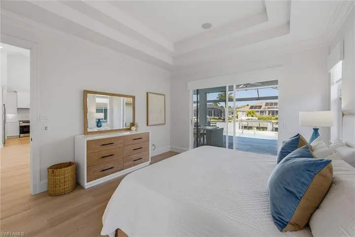 Bedroom with light wood-style floors, crown molding, access to exterior, and a tray ceiling