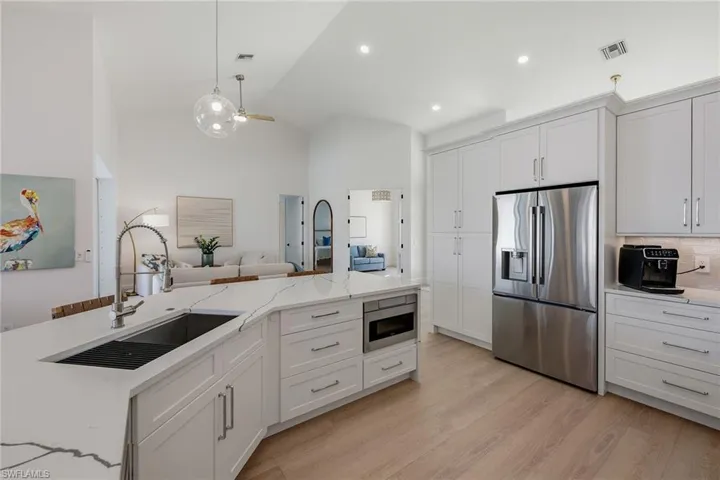 Kitchen with stainless steel fridge, white cabinets, a ceiling fan, lofted ceiling, and light stone counters