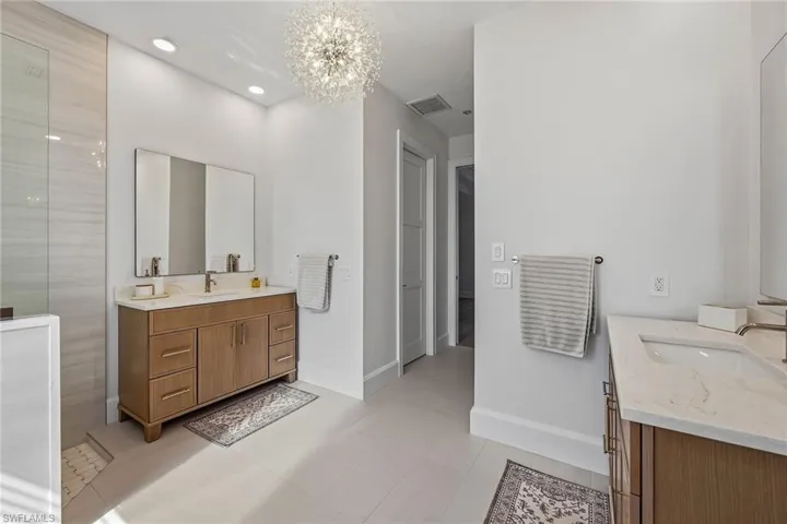 Bathroom with two vanities, a chandelier, and a tile shower