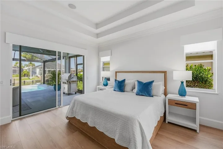 Bedroom featuring a sunroom, access to exterior, light wood finished floors, a raised ceiling, and ornamental molding